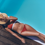 woman in swimwear covering face with hat while sunbathing by the pool