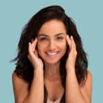 Smiling young woman with facial lift marking lines massaging her face, symbolizing cosmetic surgery, facial rejuvenation, and anti-aging treatments such as fat grafting