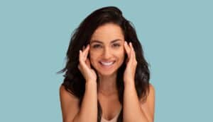 Smiling young woman with facial lift marking lines massaging her face, symbolizing cosmetic surgery, facial rejuvenation, and anti-aging treatments such as fat grafting