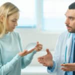 Cosmetic surgeon showing female patient breast implant samples while discussing breast implant replacement surgery in modern clinic